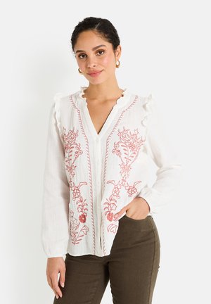 Blouse blanche avec broderies florales rouges, col froncé et fermeture à boutons sur le devant. Manches longues avec poignets froncés, texture légère.
