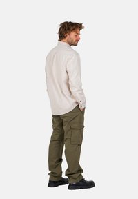 Helles beige Langarmhemd kombiniert mit olivgrünen Cargo-Hosen. Die Hose hat mehrere Taschen. Tragen Sie dazu schwarze klobige Schuhe.