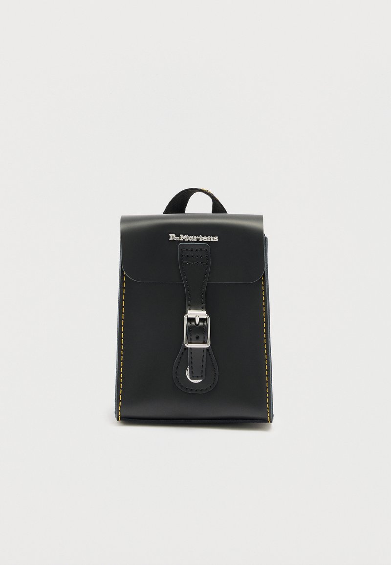 Μαύρο δερμάτινο σακίδιο Dr. Martens με ασημί κούμπωμα, κίτρινο ράψιμο στα πλευρά και χειρολαβή στο πάνω μέρος, σε απλό λευκό φόντο.