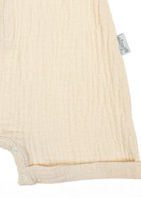 Jasnobeżowy muślinowy pajacyk z małymi zatrzaskami, teksturowaną tkaniną i miękkimi brzegami, z naszywką z nazwą marki.