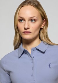 Ljusblå polo tröja med krage, med en knäppt placket och en liten broderad logotyp på bröstet. Tillverkad av texturerad bomullstyg.