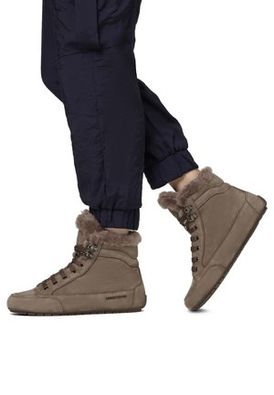 Baskets montantes en cuir marron avec un col en fausse fourrure, lacets marron et semelle en caoutchouc plate. Portées avec un pantalon de jogging bleu marine.