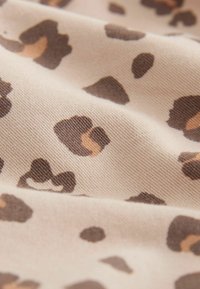 Ljusbeige tyg med ett leopardmönster som har mörkbruna och ljusbruna fläckar, med en slät, texturerad yta.