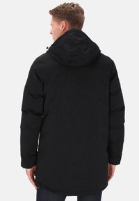 Giacca a vento nera con cappuccio, con finitura strutturata, maniche lunghe e orlo posteriore leggermente più lungo. Nessun dettaglio hardware visibile.