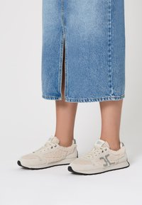 Sneaker beige con dettagli in pelliccia texure, lacci bianchi e logo grigio. Suola in gomma, materiale morbido e design della punta arrotondato.