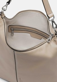 Beżowa skórzana torebka na ramię z zamknięciem na zamek błyskawiczny na górze, o gładkiej fakturze i wewnętrznej kieszeni zamykanej na zamek. Posiada metalowe elementy i usztywniony kształt.