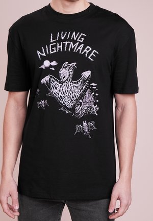T-shirt noir avec texte blanc "LIVING NIGHTMARE", présentant une figure fantomatique, des chauves-souris, la lune et une illustration d'une maison hantée.