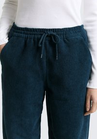 Navy corduroy joggers met een trekkoord in de taille, met verticale ribbelstructuur en zijzakken. Gestyled met een aangesloten witte top.