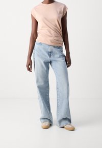 Top corto de manga corta en rosa claro combinado con jeans sueltos de mezclilla azul claro y zapatillas beige, presentando un diseño relajado y una textura suave.