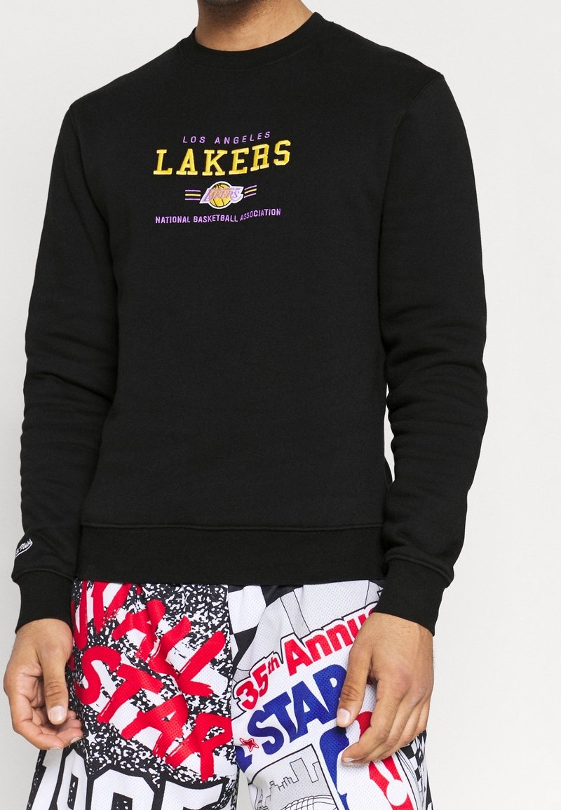 Sweat-shirt noir avec graphisme des Los Angeles Lakers en jaune et violet ; équipé de poignets et d'un ourlet côtelés. Associé à un short à motifs.