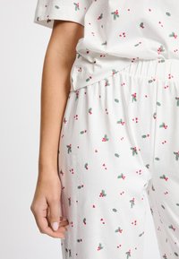 Conjunto de pijama de algodón blanco con un estampado disperso de hojas verdes y corazones rojos. Corte relajado con una cinturilla elástica.