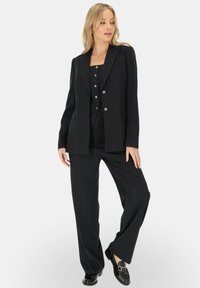 Czarny garnitur w paski, składający się z dopasowanej marynarki i szerokich spodni. Posiada srebrne guziki i zorganizowany krój. Matowe wykończenie.