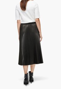 Falda midi plisada negra hecha de un material brillante con una cintura ajustada, combinada con botas tobilleras. Líneas limpias y diseño estructurado.