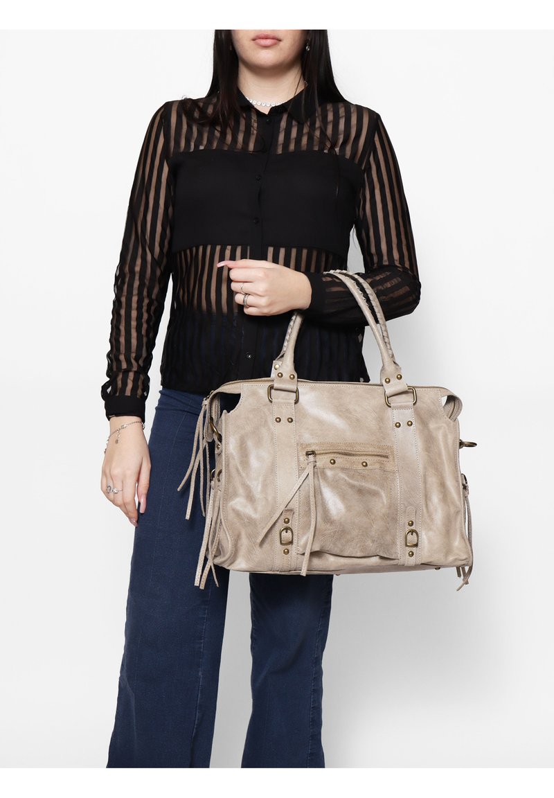 Sac à main en similicuir beige avec deux poignées supérieures, poche avant zippée et détails à franges. Texture lisse, silhouette structurée et accents métalliques.