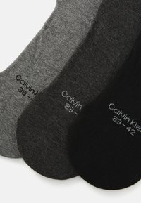 Tre paia di calzini di cotone in grigio chiaro, grigio scuro e nero. Ogni paio presenta punte rinforzate, una texture liscia e etichette di dimensione sui lati.