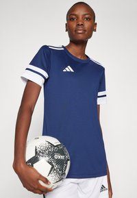 Marineblå treningsskjorte med hvite detaljer og tre striper på ermene, kombinert med en svart og hvit mønstrete fotball.