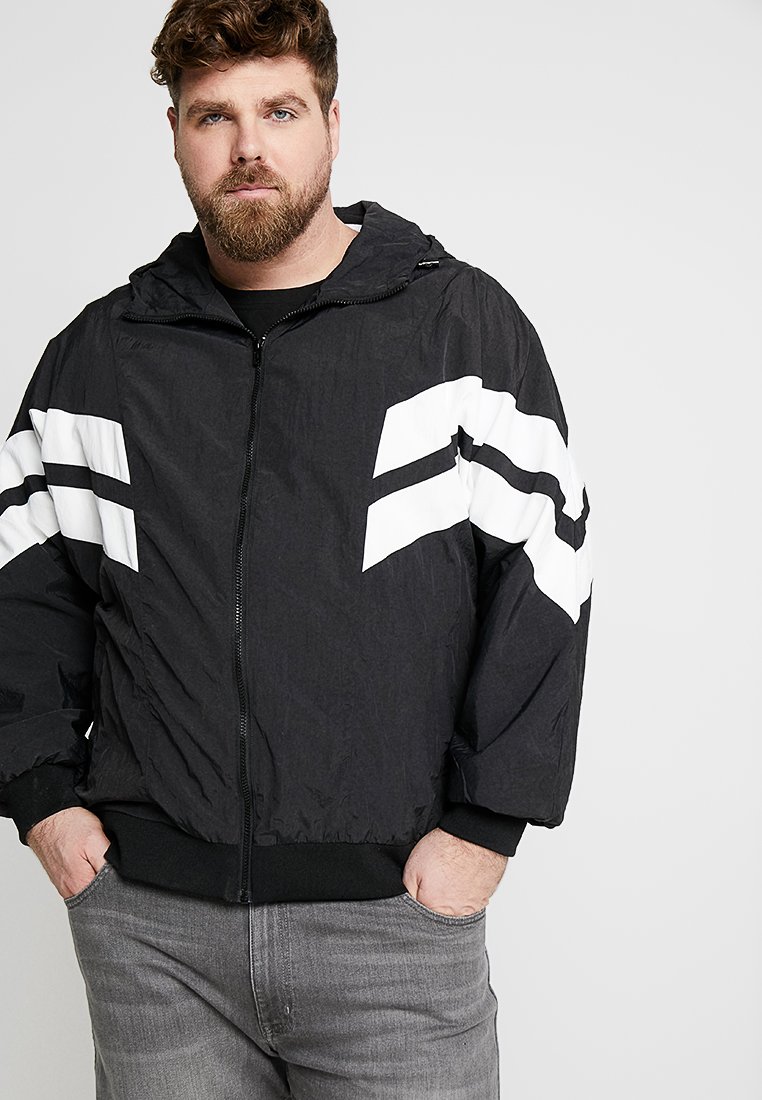 Sort zip-up jakke med hvide grafiske striber på ærmerne, lavet af letvægtsstof, med hætte og elastiske manschetter.