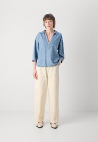 Top in denim con scollo a V e maniche ampie, abbinato a pantaloni larghi color crema e ballerine beige, che evidenziano un look casual e rilassato.