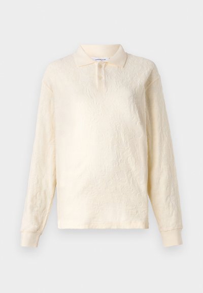 Polo a maniche lunghe color crema con tessuto texture, colletto a tre bottoni e maniche con polsini, caratterizzato da un delicato motivo floreale.