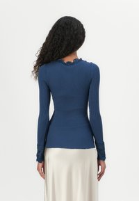 Top de manga longa em tecido canelado azul marinho com rendas nas mangas e na gola. Design ajustado, textura suave e comprimento até a metade das costas.