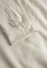 Light gray long-sleeve shirt with a button-down collar, featuring two creamy-white buttons and soft, textured fabric.
