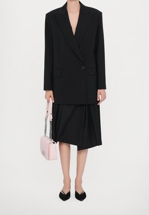 Černý oversize blazer a plisovaná sukně, doplněné růžovou kabelkou s řetízkem. Černé špičaté baleríny dotvářejí vzhled.