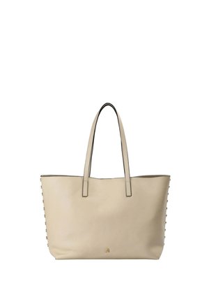 Bolso tote de cuero beige con asas largas, tachuelas doradas a lo largo de los lados y pequeño detalle de calavera dorada en la base.