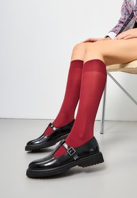 Zwarte patenten leren schoenen met een uitsnedeontwerp, vergezeld van bourgondische knie-hoge sokken. Gladde textuur, minimalistische gespsluiting.