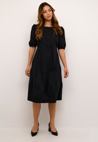 Robe noire mi-longue avec des manches bouffantes, décolleté carré et boutons sur le devant. Fabriquée en tissu texturé, elle offre une coupe décontractée.