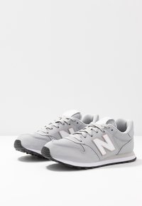 Graue Sportschuhe mit einem Obermaterial aus glattem Leder und Mesh, ausgestattet mit einem weißen Logo, Schnürsenkeln und einer schwarzen Gummisohle.