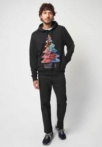 Sudadera negra con un gráfico colorido de un árbol de Navidad estilizado, combinada con pantalones negros y zapatillas. Material suave, corte relajado.