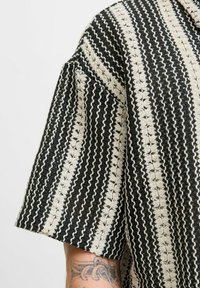 Camisa a rayas en negro y crema hecha de tejido texturizado. Presenta mangas cortas y un corte holgado, con un patrón tejido en todo el tejido.
