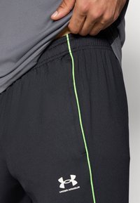 Μαύρο αθλητικό παντελόνι με στενή εφαρμογή, που διαθέτει έντονη πράσινη πλαϊνή ρίγα και ελαστική μέση. Εμφανίζεται το λογότυπο Under Armour.