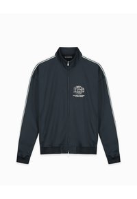 Donkerblauwe ritjacket van gladde stof, met witte zijstrepen, een klein logo op de borst en geribbelde boorden en onderkant.