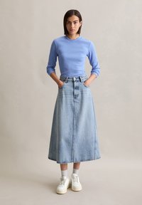 Camiseta de manga larga de canalé azul claro combinada con una falda de mezclilla azul claro de tiro alto y hasta el tobillo, y zapatillas blancas con suelas gruesas.