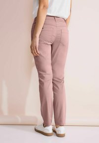 Růžové kalhoty ze směsi bavlny se slim fit střihem, obsahující zadní kapsy a decentní detaily prošívání, doplněné bílými teniskami na světlém pozadí.