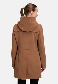 Bruine, capuchonjas gemaakt van een gestructureerd wolachtig materiaal. Ontworpen met een getailleerde silhouet en minimale stiksels details aan de achterkant.