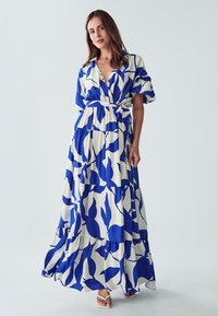 Maximekko valkoisesta kankaasta sinisillä abstrakteilla lehtikuosisilla, jossa on kauluskortti, lyhyet hihat, vyötärölle sidottu vyö ja kerrostettu helma.