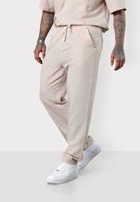 Light beige patterned joggers with a drawstring waistband, side pockets, and elastic cuffs, paired with white sneakers.