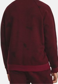 Burgundy idrottströja med ribbad textur, med rundad halsringning, raglanärmar och en enfärgad midja, utan synliga logotyper.