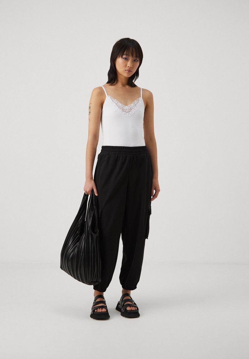White camisole with lace trim paired with black elastic waist tapered pants and black strappy sandals, holding a black pleated tote bag.