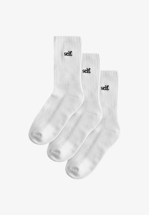 Three pairs of white cotton socks with ribbed texture, featuring black "self." logo on the upper side. Standard crew length.