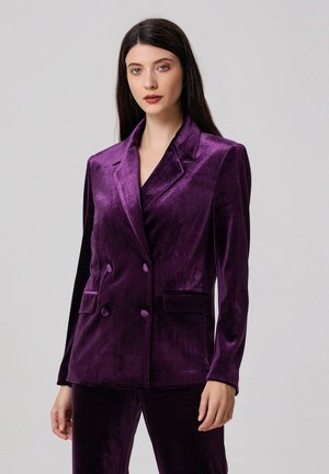 Blazer double boutonnage en velours violet avec un revers aigu, deux poches avant et un tissu texturé avec une douce brillance.