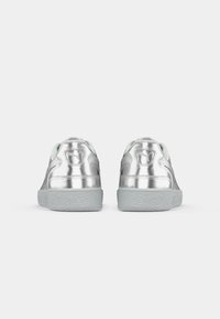 Et par sølvmetallic sneakers med teksturerede grå såler set fra baggrunden på en hvid baggrund.