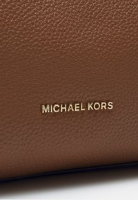 Brązowa skórzana torba z teksturowaną powierzchnią i wyraźnie widocznym złotym logo "MICHAEL KORS".