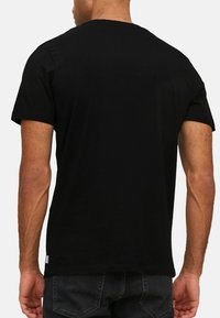 T-shirt nera in cotone con maniche corte, scollatura tonda, texture liscia e una piccola etichetta all'orlo, vista dal retro.