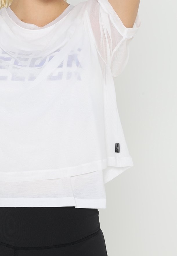Vit nätoberdel med kort ärm och lös passform, med ett subtilt grafiskt mönster, lagerdesign och en liten logotags vid fållen.