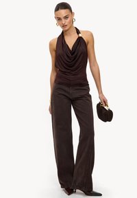 Haut à col bénitier en satin marron, associé à un pantalon marron à jambes larges. Les accessoires comprennent un petit sac à main tissé et des boucles d'oreilles créoles.