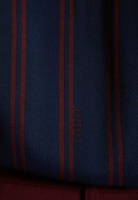 Mornarska tkanina s bordo prugama, koja se odlikuje glatkom teksturom i suptilno ušivenim imenom branda "Otto".