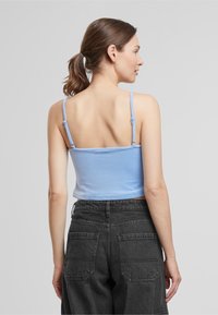 Top corto de tirantes finos en azul claro, combinado con unos vaqueros negros de cintura alta que tienen bolsillos traseros y detalles de costura.